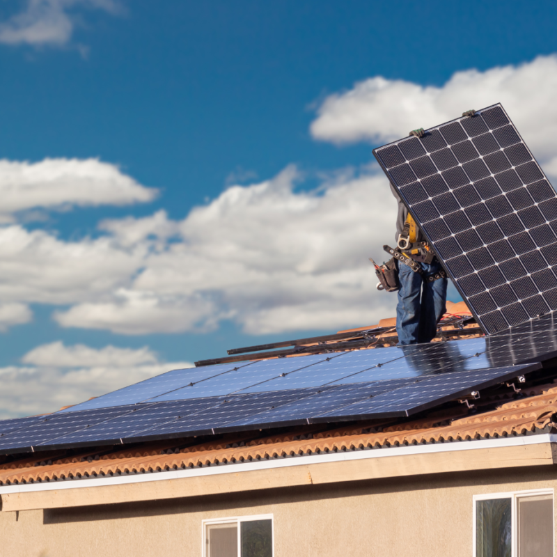 Two workers installing solar panels on a tiled roof under a bright blue sky, representing the best solar installation company on Sunshine Coast – TMEC Services.
