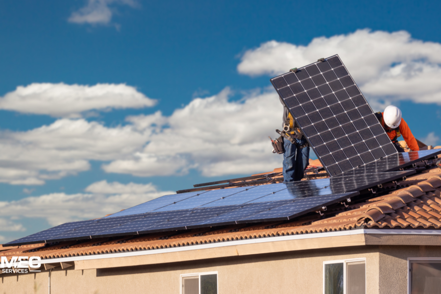 Two workers installing solar panels on a tiled roof under a bright blue sky, representing the best solar installation company on Sunshine Coast – TMEC Services.