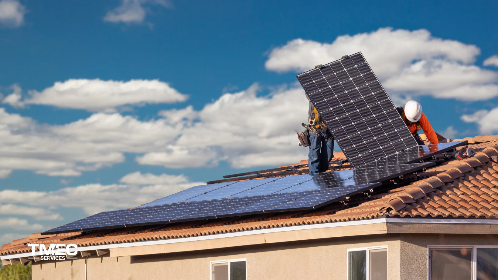Two workers installing solar panels on a tiled roof under a bright blue sky, representing the best solar installation company on Sunshine Coast – TMEC Services.